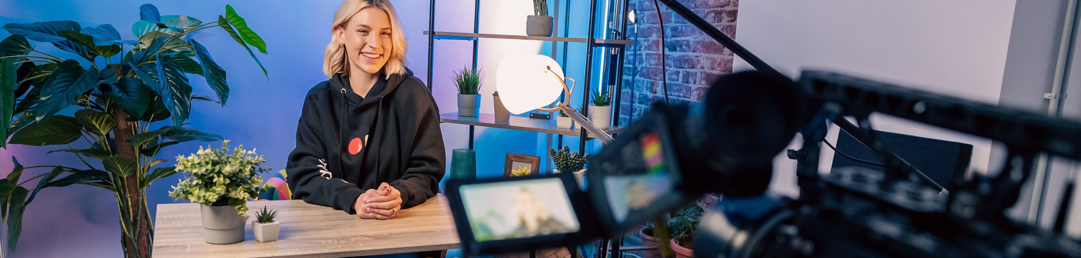 A small business owner creating video content for tiktok. They are sat behind a desk with studio style lighting and a video camera in the foreground.