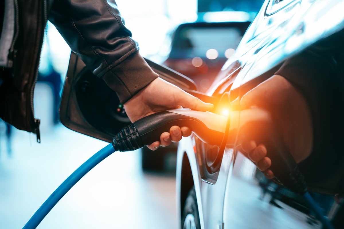 Image of a man plugging in a EV charger to his vehicle with a futuristic light behind it illustrating the growth of electric vehicles