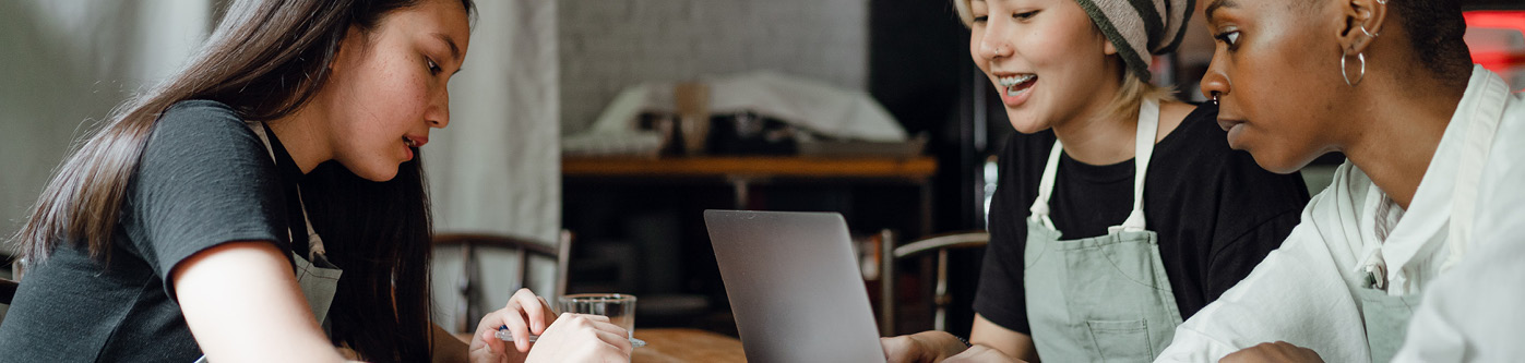 3 female employees looking at energy saving tips on laptop in cafe